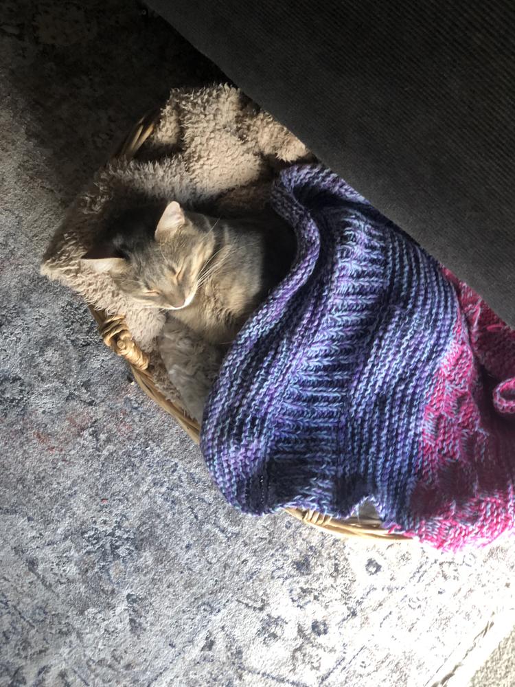 A grey cat sleeps soundly under a handmade blanket.